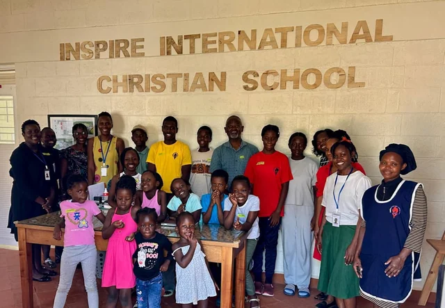 Adults and children together beneath the Inspire International Christian School sign